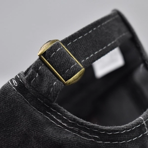 Detail of vintage bronze metal buckle and contrast stitching on black baseball cap