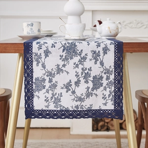 Blue floral linen table runner with navy lace edges on a wooden dining table