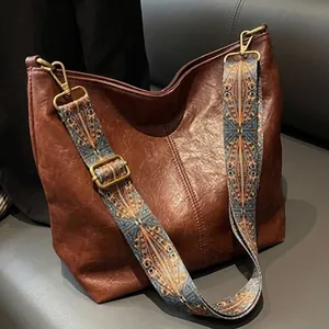 Detail view of the wide ethnic pattern shoulder strap on a brown vintage crossbody bag