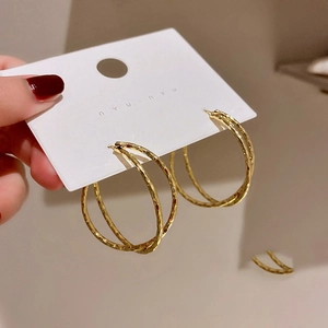 Detail of gold double-hoop earrings with hammered texture on a model hand