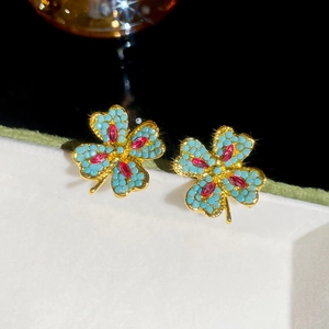 Detailed macro view of gold-tone four-leaf clover stud earrings with blue beads