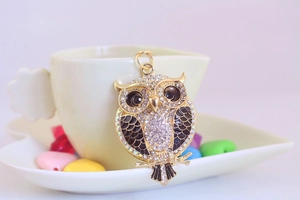 Close-up of golden owl keychain with crystal rhinestones on a decorative ceramic cup