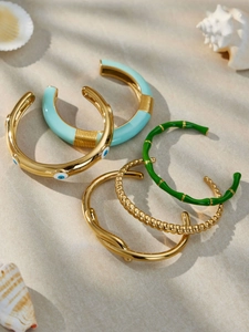 Dettaglio dei bracciali dorati con occhio smaltato e conchiglie su sabbia marina