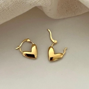 Detail of polished gold heart-shaped huggie earrings on a soft cream fabric background