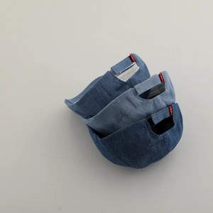 Dettaglio dei cinturini regolabili e delle etichette rosse su tre berretti in denim
