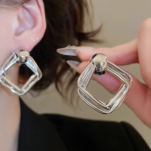 Close-up of geometric layered silver square hoop earrings worn by a model