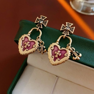 Dettaglio macro di orecchini gotici vintage con cuore in smalto viola e gigli dorati