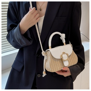 Detailaufnahme der gewebten Strohhandtasche mit weißer Lederklappe und goldener Blumenschnalle