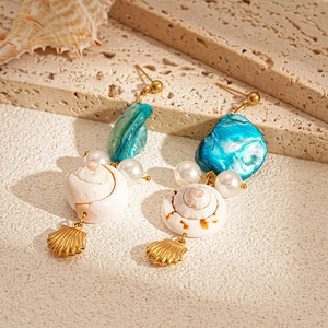 Detail of seashell drop earrings with pearls and blue accents on stone surface