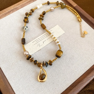 Detail of beaded necklace with tiger eye stone drop pendant on linen surface
