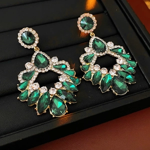 Détail de boucles d'oreilles dorées avec pierres émeraude et strass scintillants
