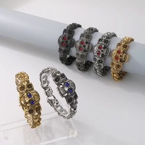 Gros plan de bracelets crâne punk avec yeux en gemmes rouges et bleues en finitions or et argent