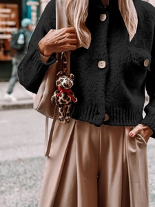 Detail of a leopard print bear charm with red bow on a beige bag and black cardigan