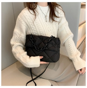 Close-up of black quilted crossbody bag with chunky acrylic chain on white sweater