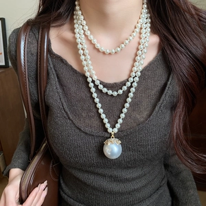 Detail of multi-layer pearl necklace with a large diamond-encrusted pendant on a model