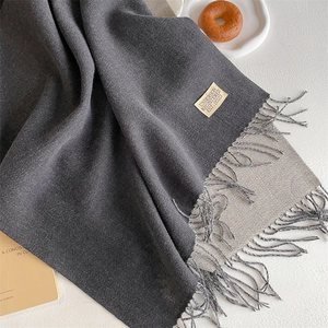 Detail of grey cashmere-like scarf with fringe edges and small branded fabric label