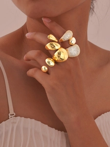 Detailed view of layered chunky gold rings and sparkling teardrop zircon ring on finger