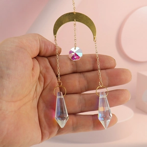 Macro view of gold moon suncatcher with rainbow crystal prisms and chains held by hand