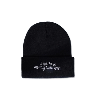 Detail view of black beanie with white 'I got here on my unicorn' slogan embroidery