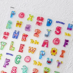 Detail von 3D-Gel-Nagelstickern mit bunten Buchstaben und Monstern auf Folie