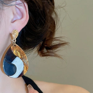 Detailed view of large teardrop earrings with black and white enamel and hammered texture