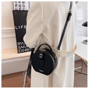 Model wearing a black leather round crossbody bag with gold fashion lettering and hardware