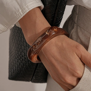 Close-up of a wide amber resin geometric bangle with marbled texture on a model wrist