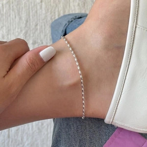 Close-up of minimalist S925 sterling silver olive bead anklet worn on model ankle