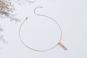 Gros plan détaillé d'un collier barre or rose avec gravure cœur et petit cristal