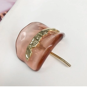 Macro detail of a translucent resin U-shaped hair pin with wave-textured gold metal accents