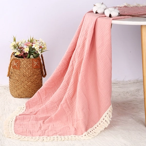 Soft pink double-layer muslin cotton baby blanket with beige tassels on a small table