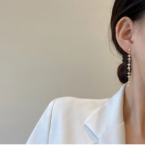 Detail shot of long gold star earrings with white zircon crystals on a model
