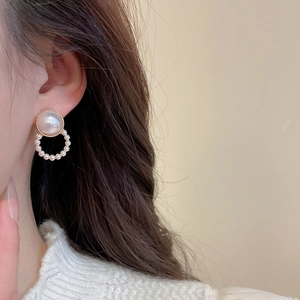 Detail showing a large pearl stud with a dangling gold circle of small pearls on a model