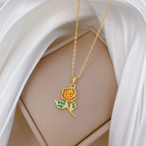 Close-up of golden rose pendant with green leaves on silk in a jewelry box
