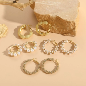 Set of four gold pearl and zircon earrings displayed on elegant textured natural stones