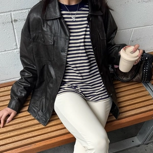 Detailaufnahme der schwarzen Lederjacke im Oversize-Stil mit blau gestreiftem Langarmshirt