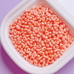Close-up of pearlized coral pink peanut shaped dual-hole beads for DIY jewelry making