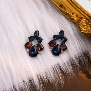 Macro shot of teardrop rhinestone earrings on white fur with vintage gold frame