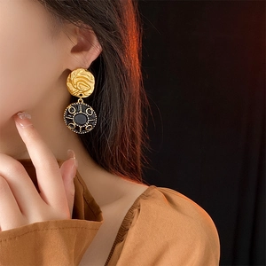 Close-up of vintage round gold and black enamel drop earrings worn by a model