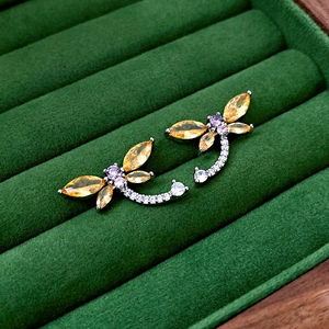 Macro shot of dragonfly stud earrings with yellow and purple zircons on green velvet