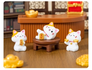 Three cute miniature fortune cats holding gold coins on a creative office desk display