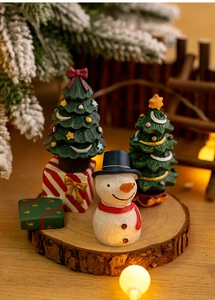 Miniature resin Christmas figurines featuring a snowman, tree, and striped gift boxes on wood