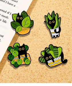 Close-up of four cute black cat and potted plant enamel pins on a cork background