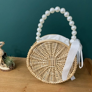 Detail of round straw bag with pearl handle, white ribbon bow and fabric lining