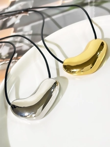Macro view of gold and silver bean pendants on black cords with a mirror polish finish