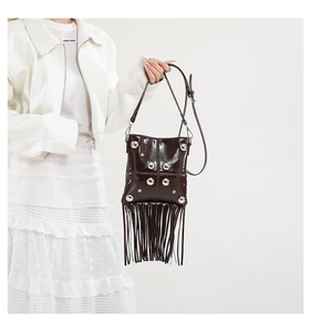 Detail of dark brown patent leather crossbody bag with silver studs and long fringe
