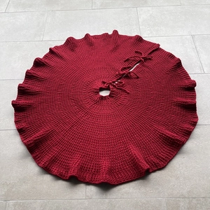 Detail of dark red chunky knit Christmas tree skirt with decorative ribbon tie closures