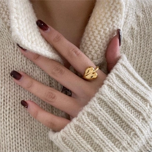 Polished gold heart-shaped ring on hand with warm winter knit sweater background