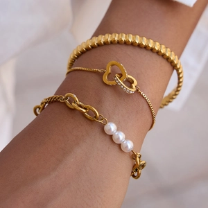 Detailed close-up of stacked gold bracelets featuring textured bangle and pearl chain
