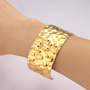 Detail shot of a wide gold-plated cuff bracelet featuring a unique hammered texture finish